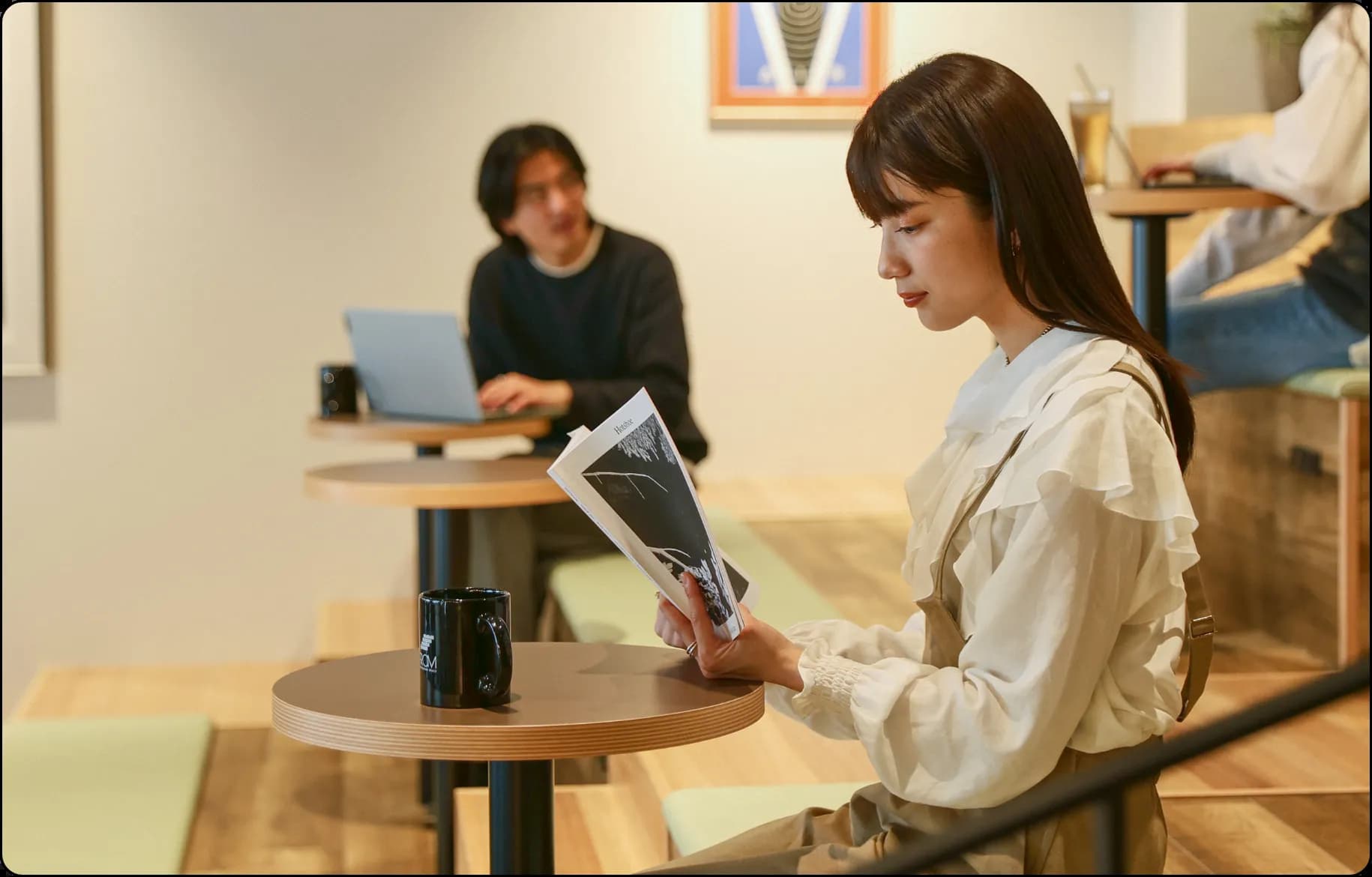 コーヒーを片手に読書している女性やその背後ではパソコンを操作している男性がいるなど作業に集中できるような雰囲気のある写真