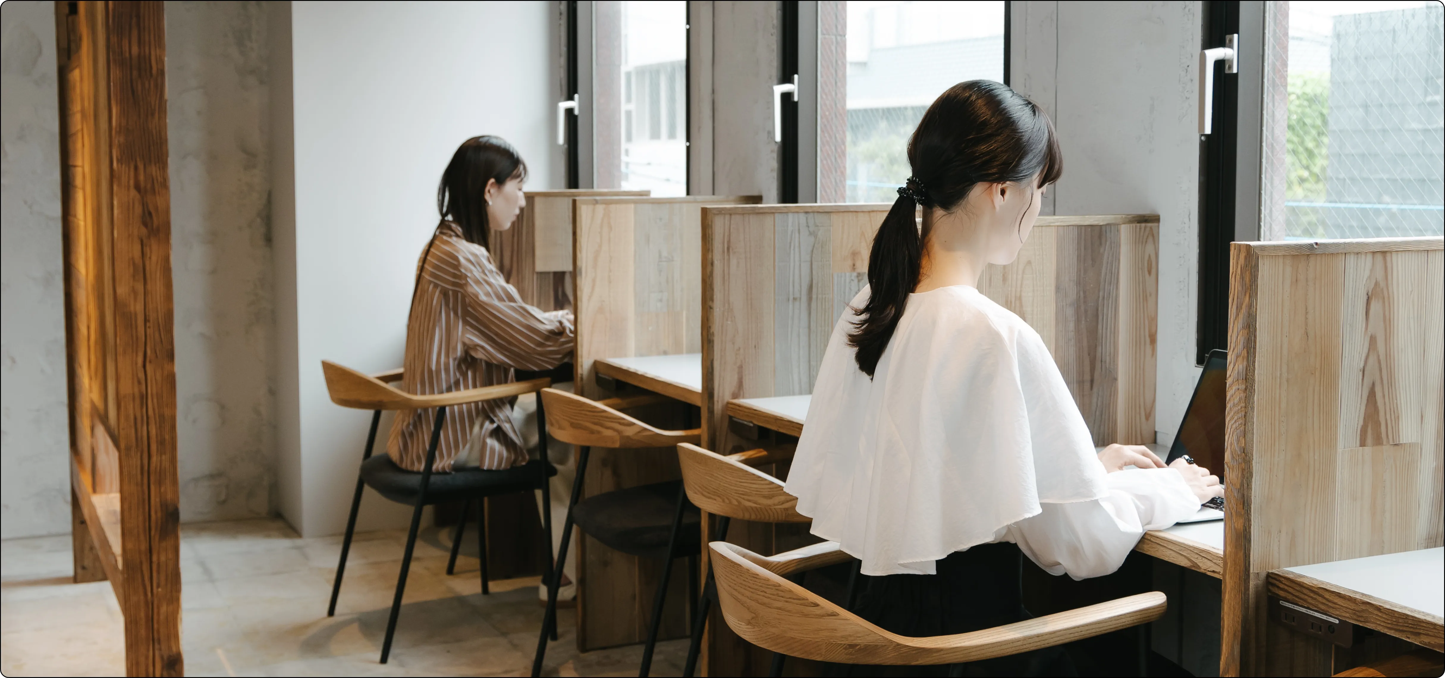 写真: 木の仕切りの間でパソコンを操作している2人の女性