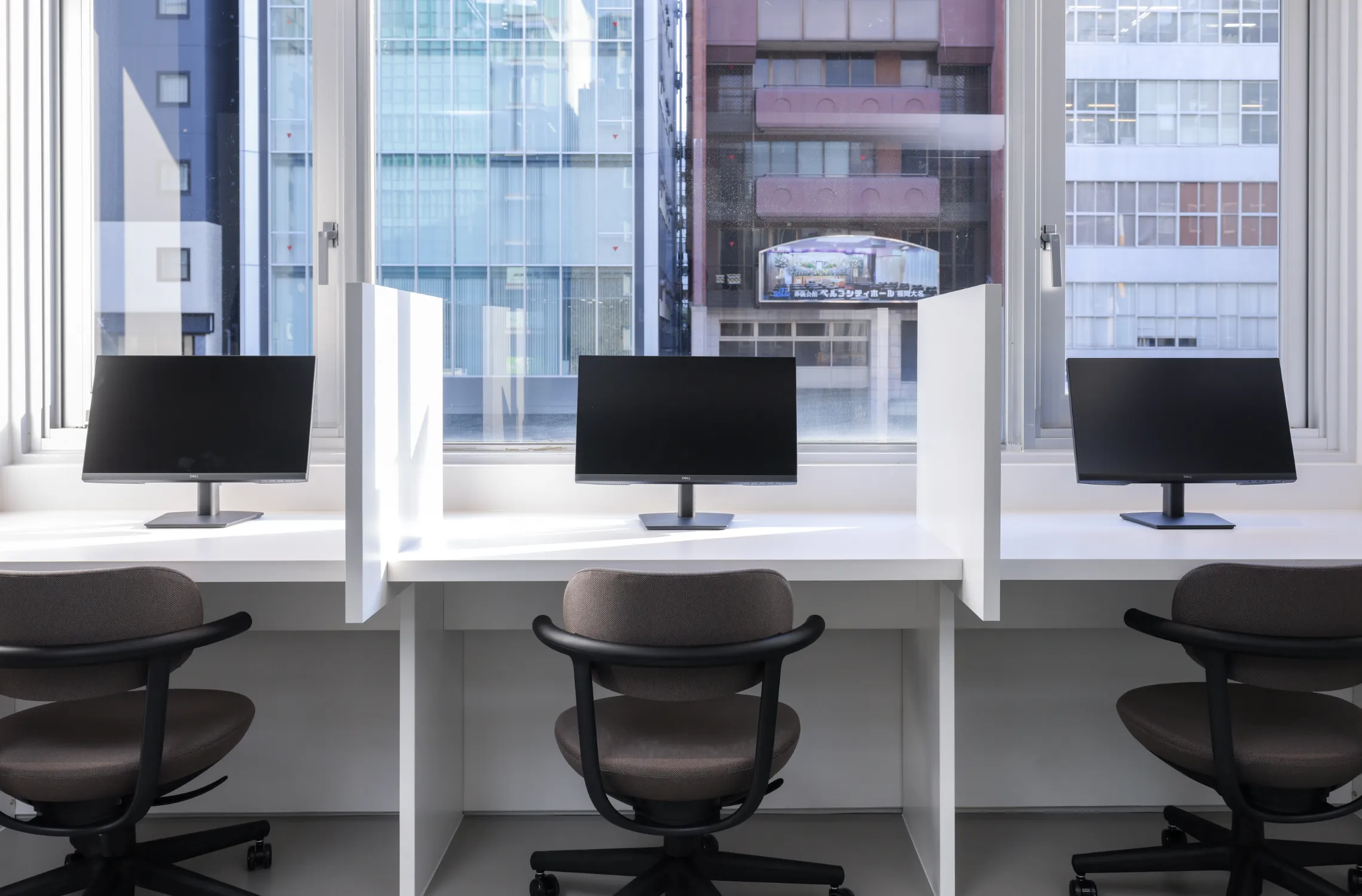 写真。窓際の仕切りのあるデスク1つ1つにモニターとオフィスチェアを完備